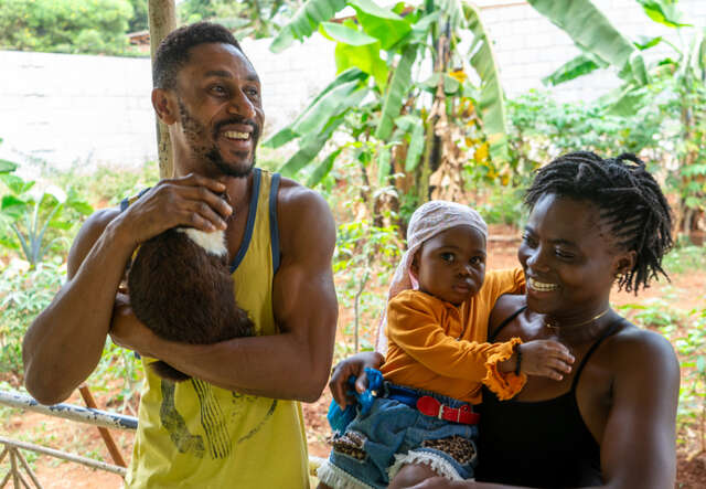 A man holding a rabbit with his wife and child in front of small allotment
